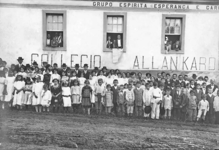 Fotografia antiga de alunos e professores diante do prédio com a inscrição Collegio Allan Kardec