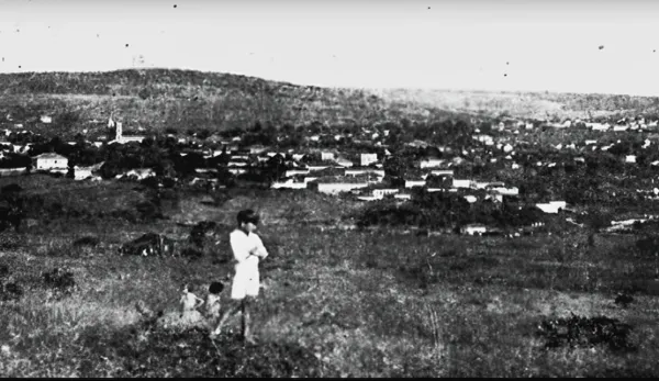 Fotografia antiga de uma criança em um campo, com a cidade ao fundo