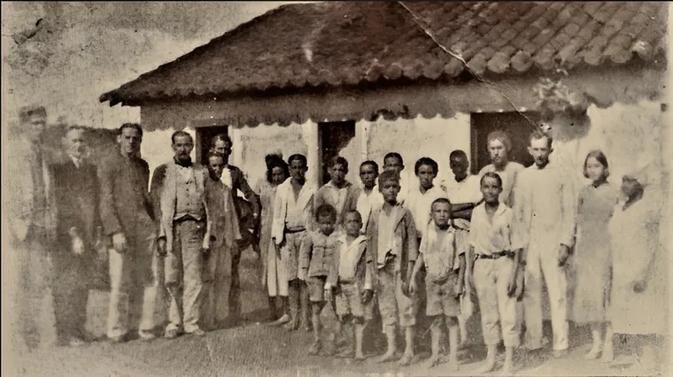 Fotografia antiga de um grupo de pessoas diante de uma casa de fazenda