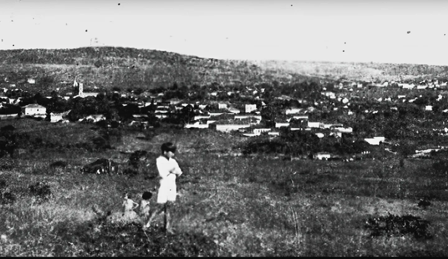 Fotografia antiga de uma criança em um campo, com a cidade ao fundo