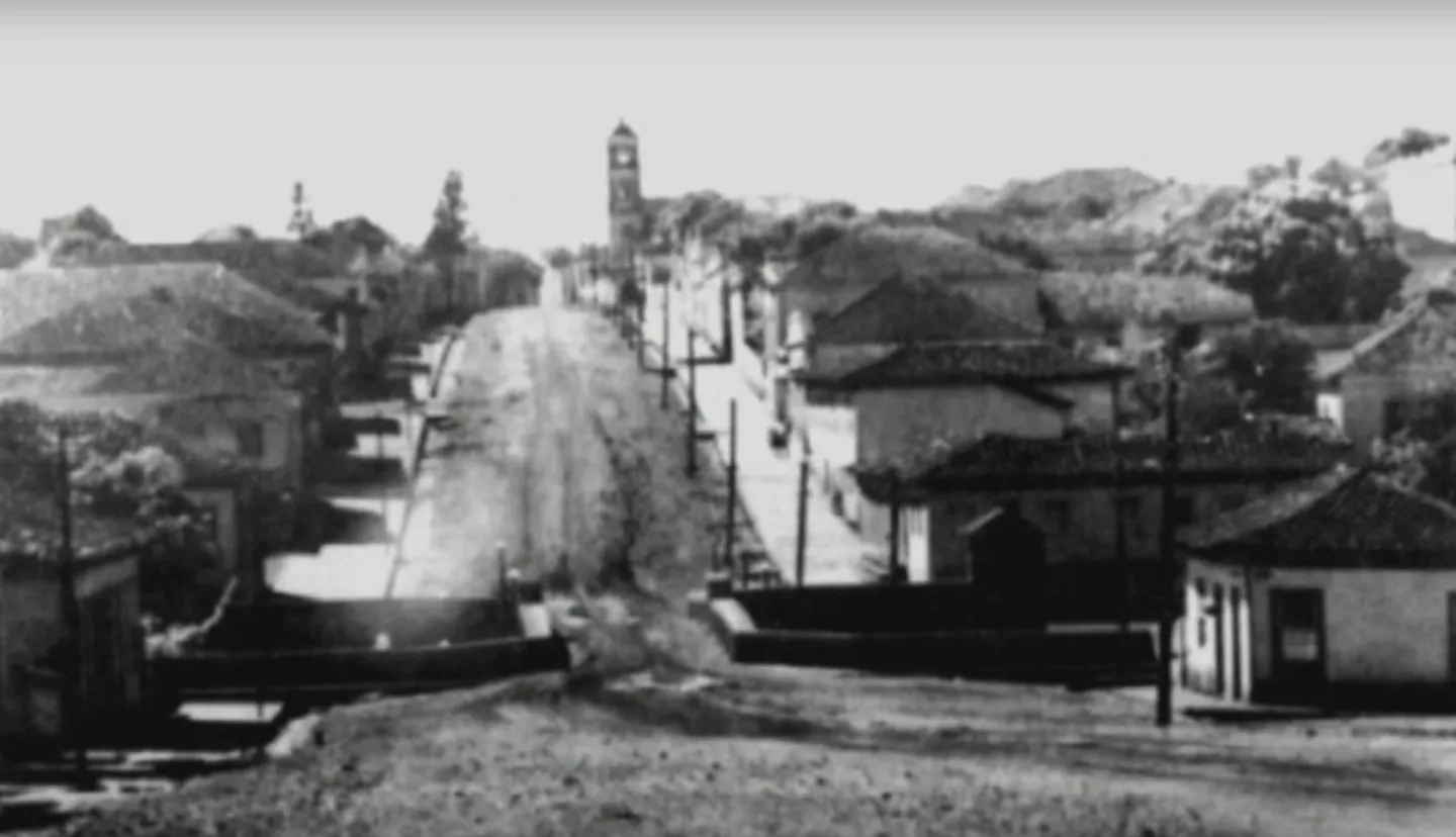Rua de Sacramento com torre de igreja, em fotografia antiga
